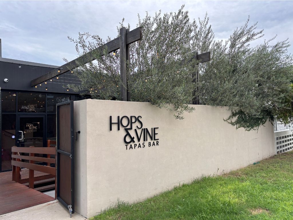 The simple exterior with its rendered walls and tall olive trees conceals much of the world inside Hops & Vine Tapas Bar, Emerald.